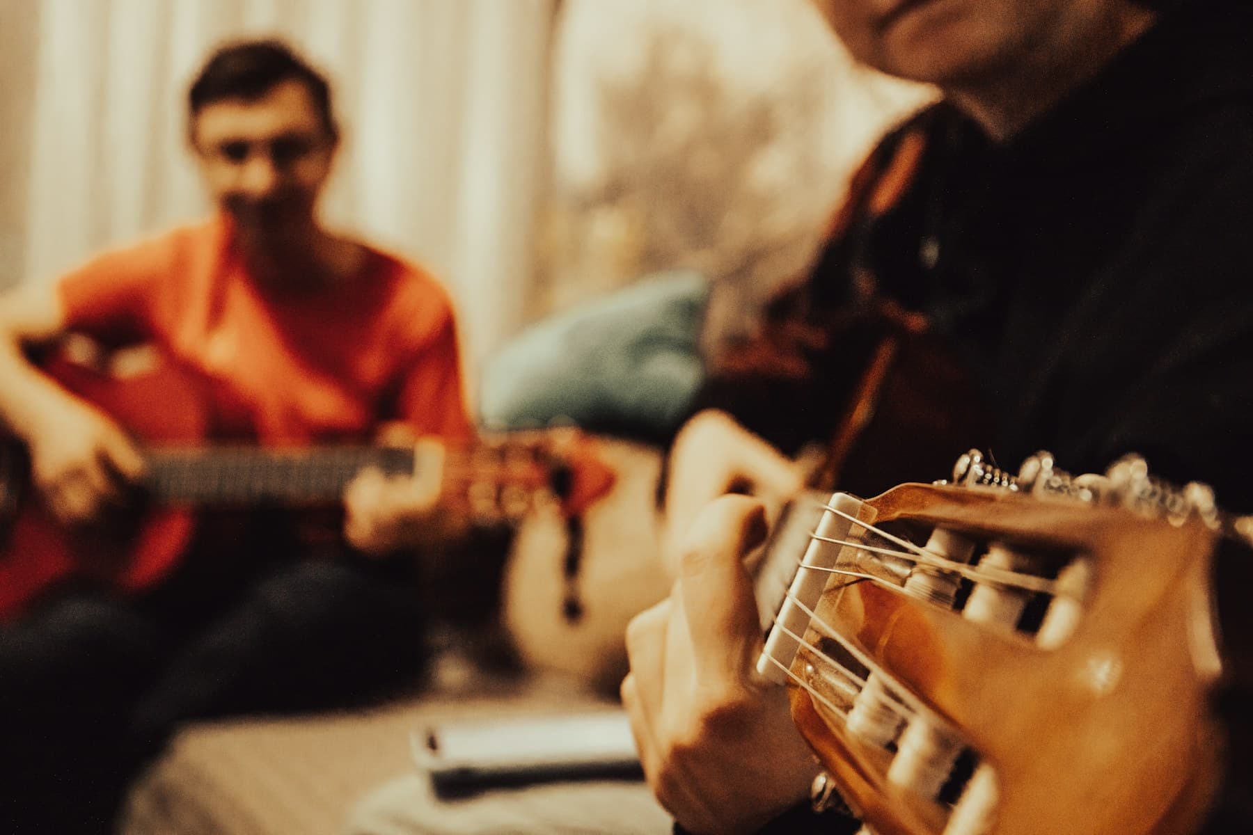 Duas pessoas tocando violão juntas em uma sala de aula com luz quente